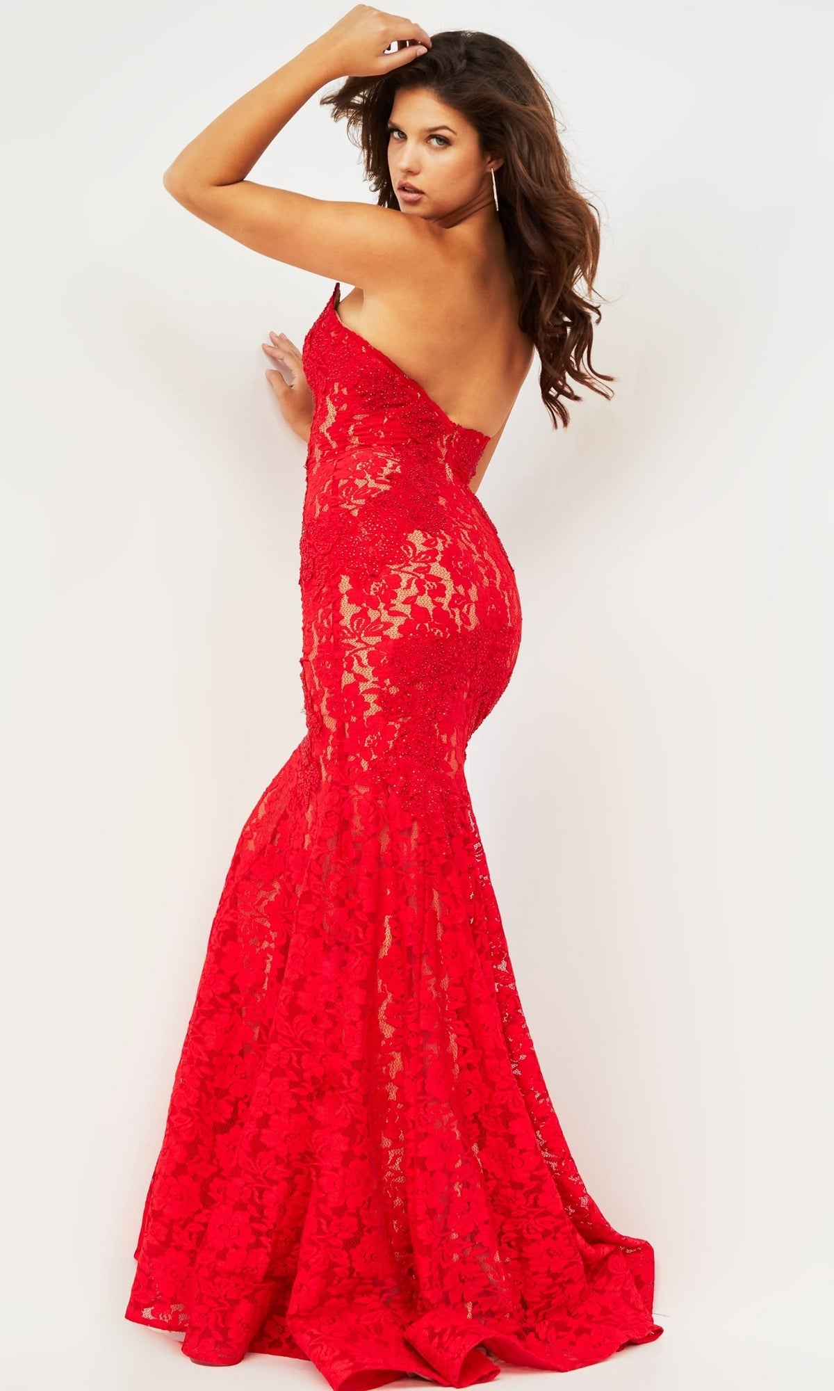 A woman poses with one arm raised and looks over her shoulder, wearing the Long Prom Dress 37334 by Jovani—a form-fitting, strapless red lace gown—against a plain white background.